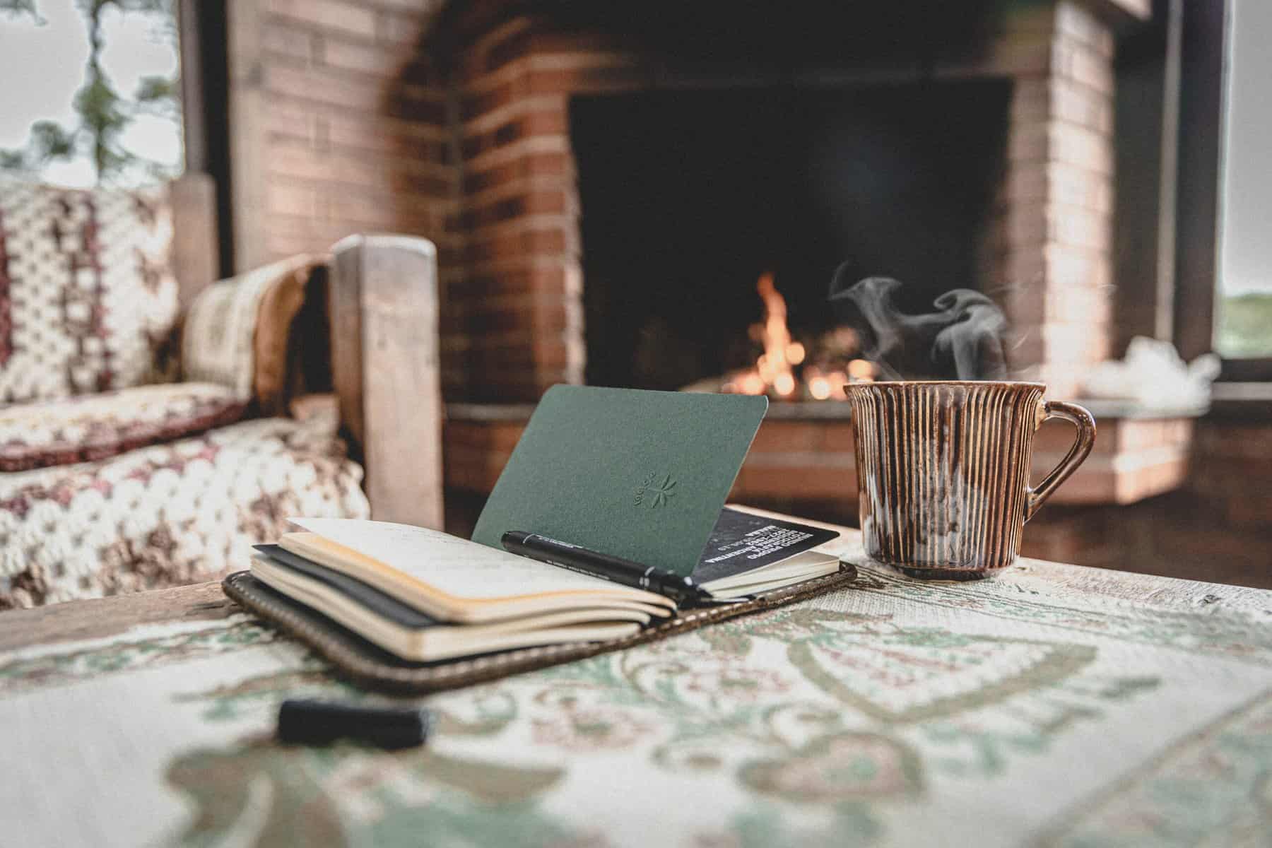 journal and cup of coffee next to a cozy fireplace