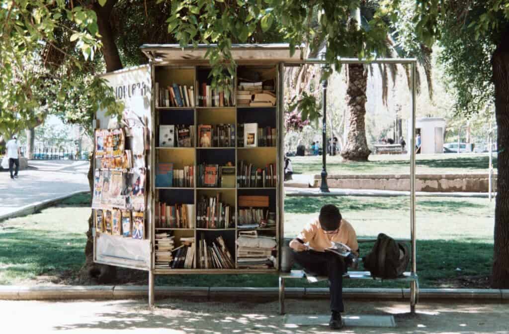 Person reading by bookshelf outdoors