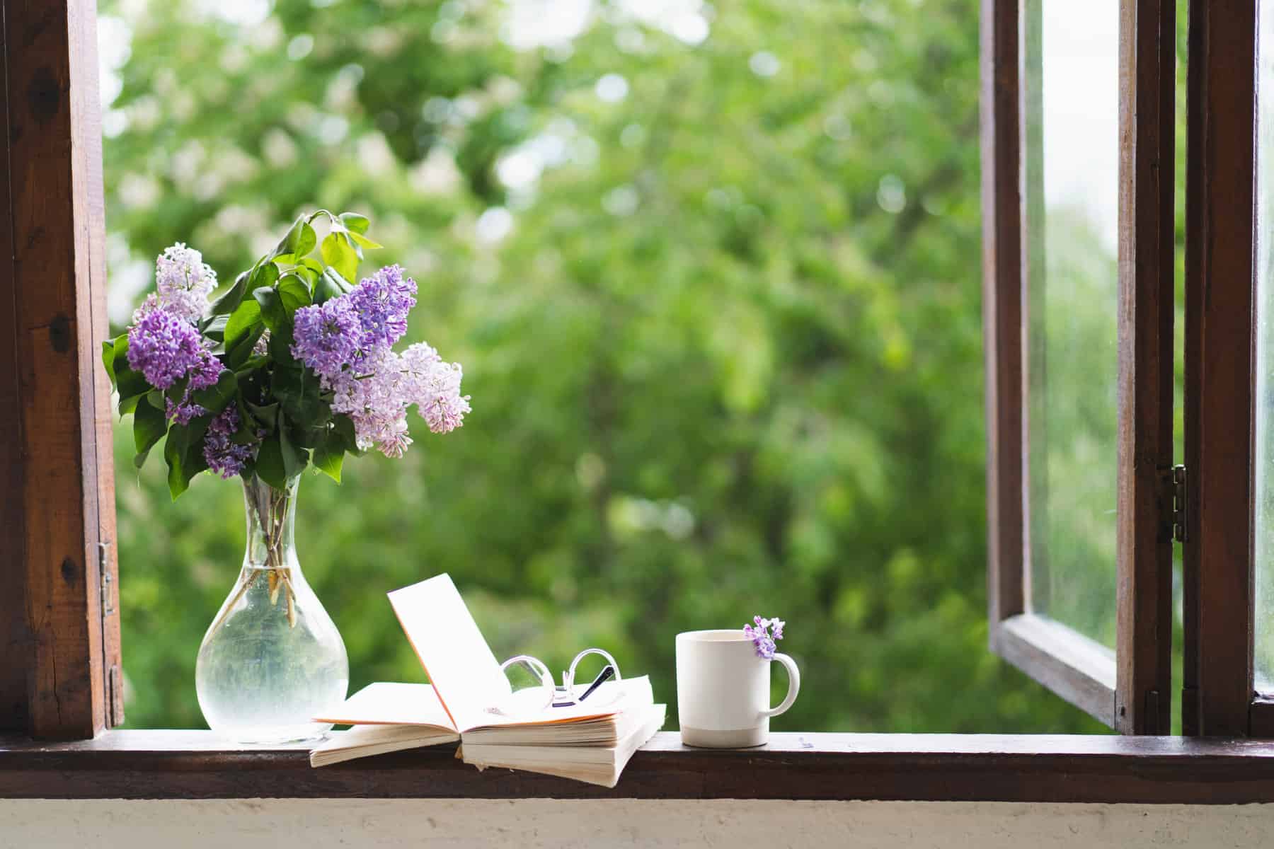 Book, glasses, cup of tea and lilac on a wooden window. Fragrant tea in the garden. Romantic concept. Vintage style