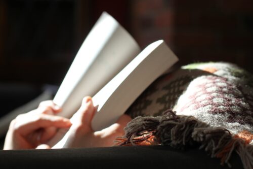 person reading a book under a cozy blanket